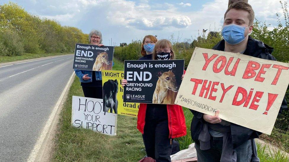 People holding signs by the side of the road.