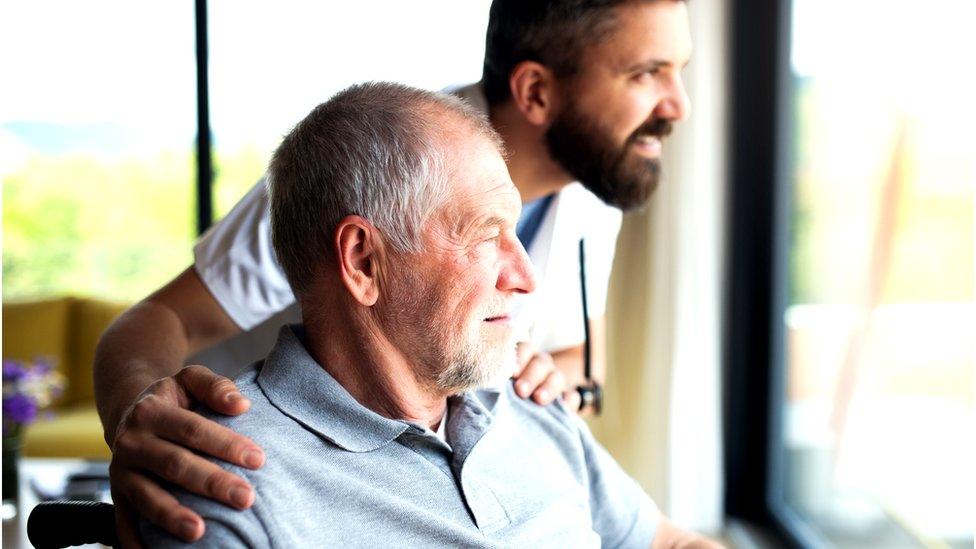 carer looks out of window with elderly man