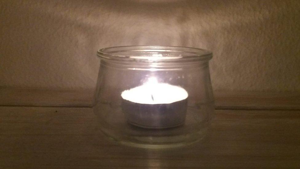 A tea light in a glass candle holder shines brightly on the 80th anniversary of Kristallnacht