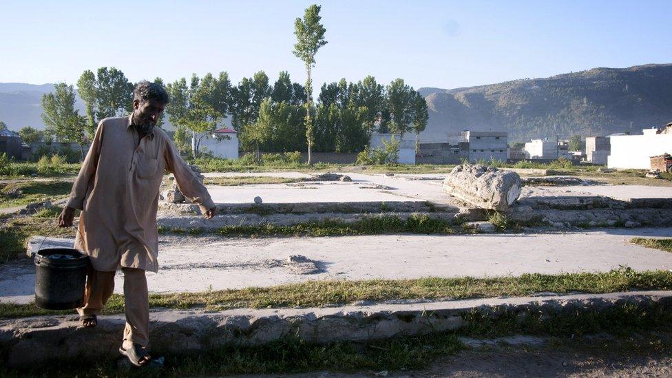 A man carrying a bucket of water makes his way across the razed compound