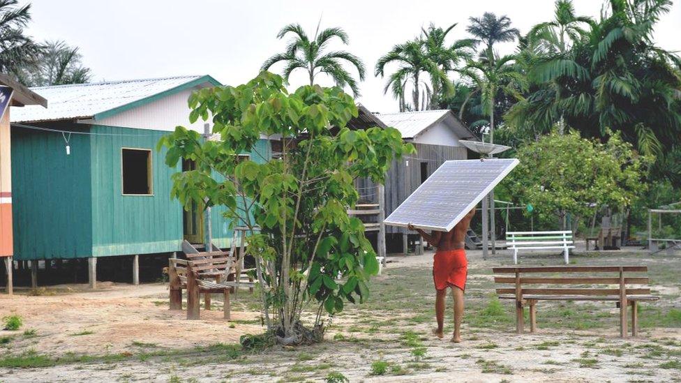 Person carries a solar power panel through a village in Brazil