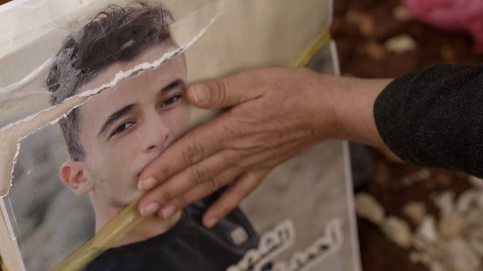 Hand of the four brothers' mother on graveside photo of one of her sons