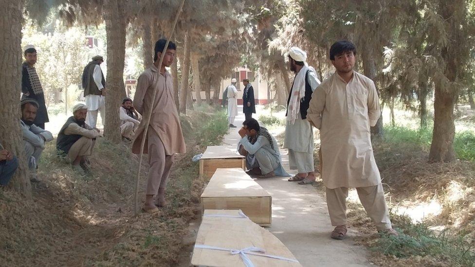 Relatives stand by side of three wooden coffins on a road