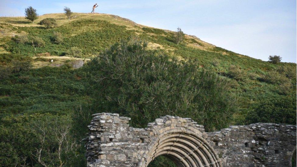 Looking up at the statue in the distance with the abbey ruins in the foreground below