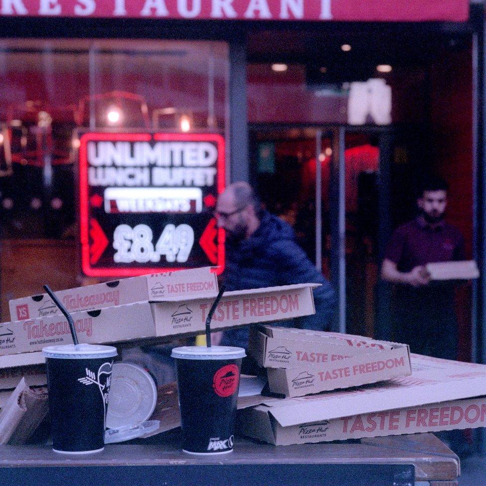 A table covered with paper cups and empty boxes outside a takeaway food shop