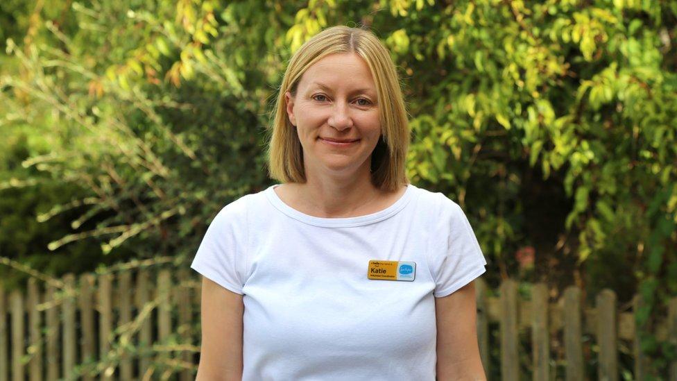 Blonde woman in white t-shirt standing in front of a green bush