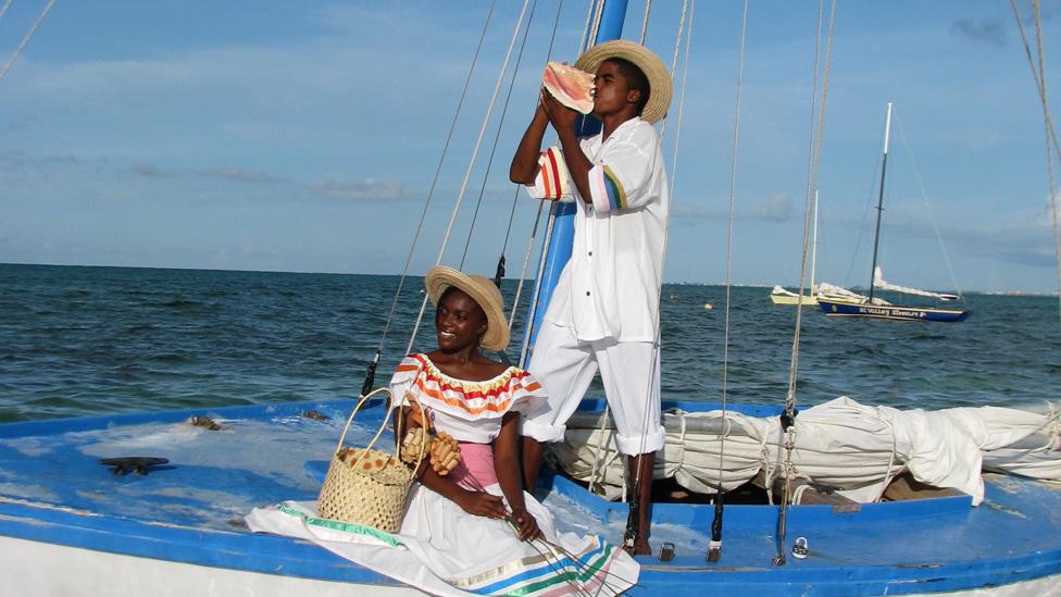 A man blows a conch while on a boat