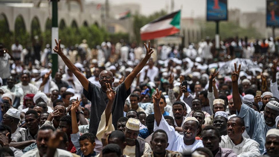 Sudanese protesters flash the victory sign ahead of a Friday prayer outside the army headquarters in the capital Khartoum on April 19, 2019. -