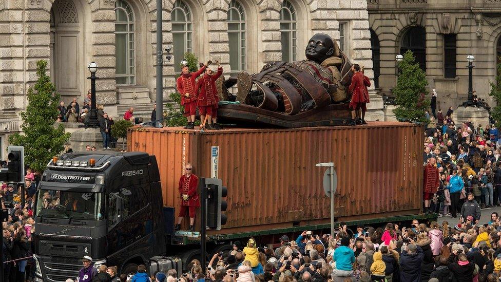 A huge puppet named Little Boy Giant is transported along the dockside