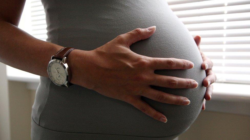 An eight month pregnant woman holds her belly, baby bump