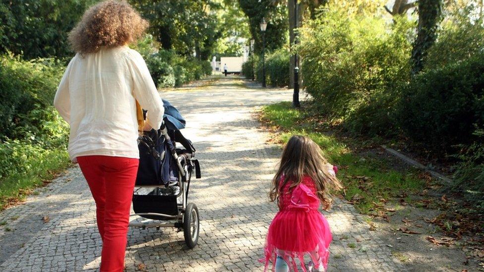 Woman pushing pram with child by her side