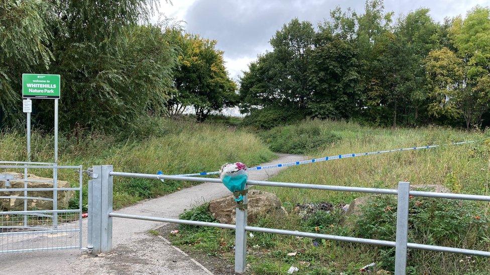 Bouquet of flowers tied to fence post next to police tape