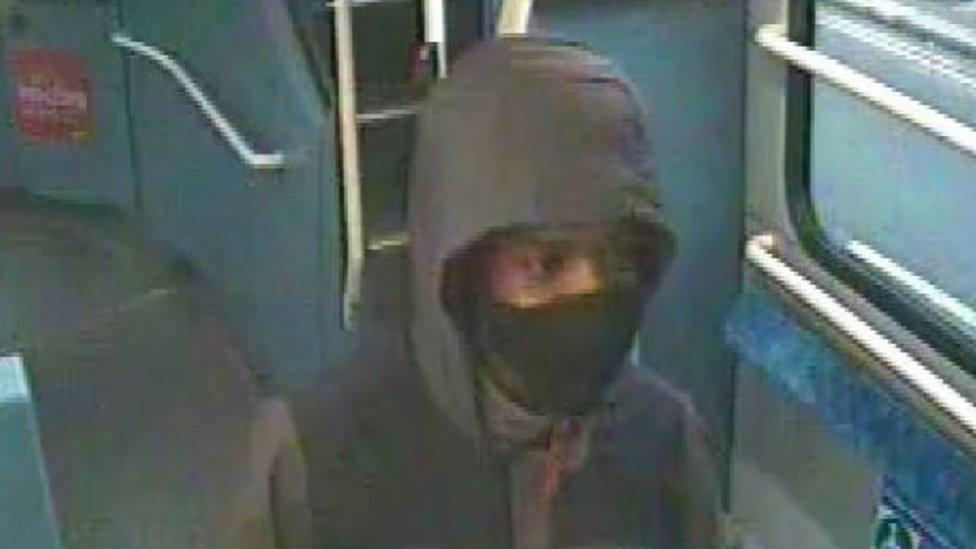 Image of the man wearing a black and grey hooded coat with a red zip and a black facemask