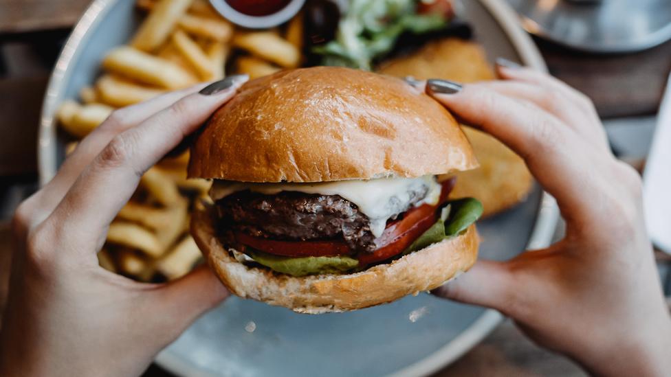 Stock image of hands holding a burger, with chips on a plate in the background