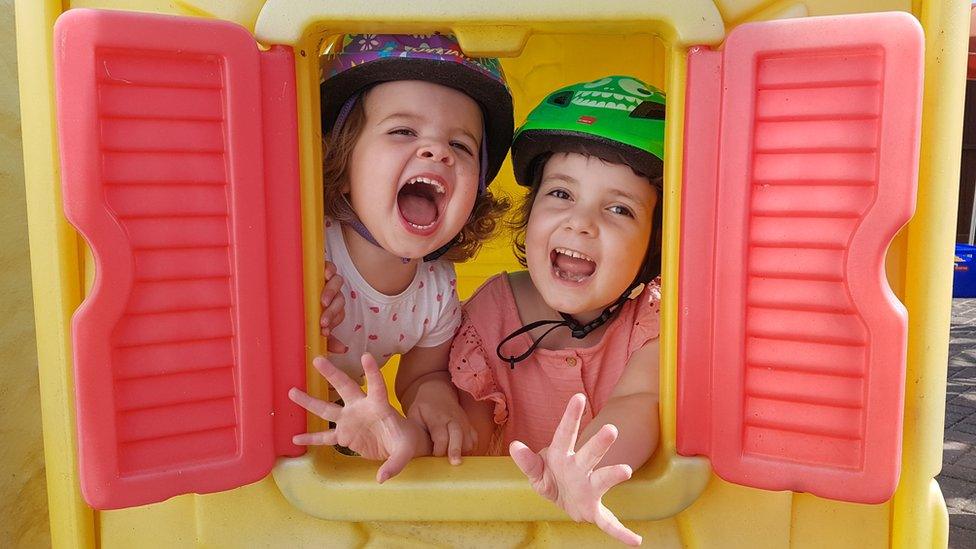 Two girls wearing cycle helmets looking through the window of a playhouse