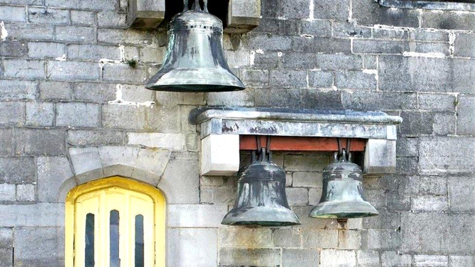 three bells on the outside of a stone wall