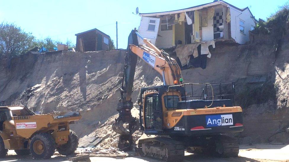 Heavy machinery on the beach clearing debris from collapsed house