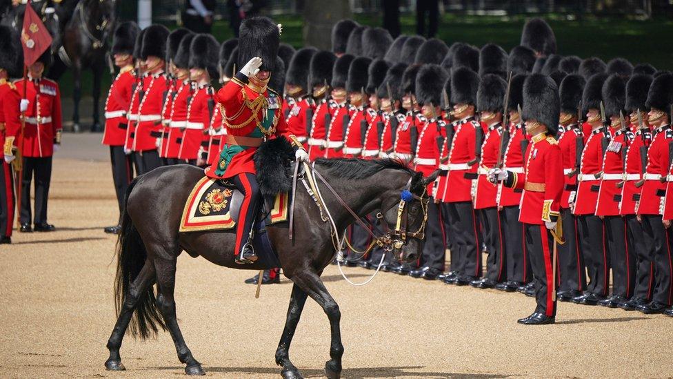 prince charles salutes troops while riding a horse