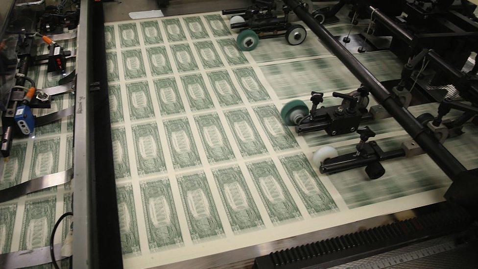 Dollar bills roll off a government printing press.