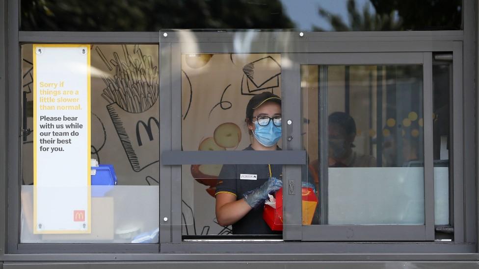 A member of McDonald's staff behind a reinforced driver thru serving window