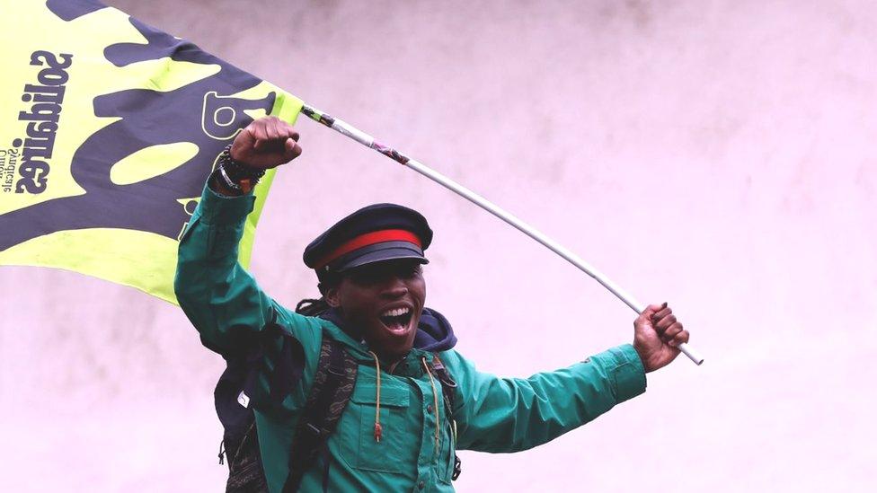 Man with fist raised laughing and holding a flag, one of hundreds of protesters against a French government project to change the status of the railroad workers