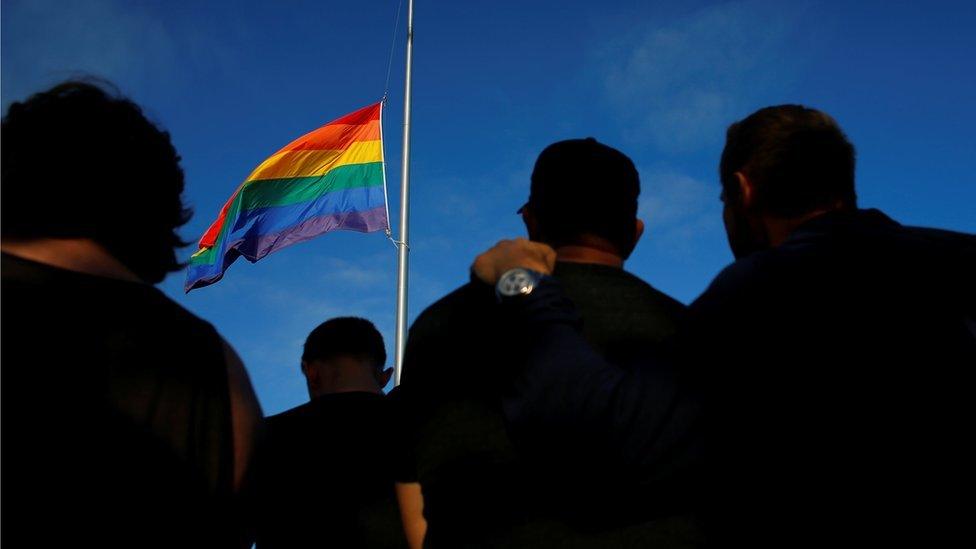 Mourners gather under an LGBT pride flag flying at half-mast for a candlelight vigil in remembrance for mass shooting victims in Orlando, from San Diego, California, U.S. June 12, 2016