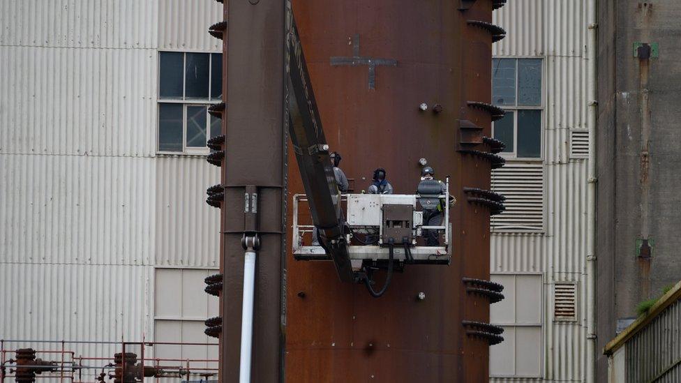 Three workers on a cherry picker next to big old buildings