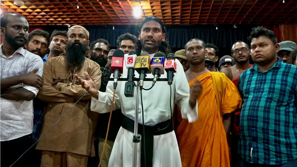 Father Jeevantha (centre) speaks at Colombo library meeting, with Wasantha Mudalige in blue-green checked shirt on far right