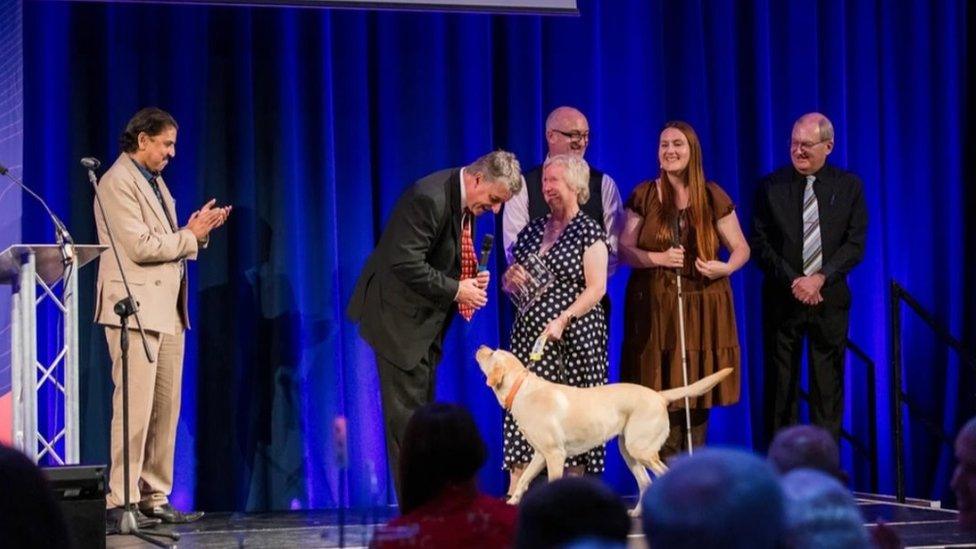 Several people, and a dog, on stage collecting an award