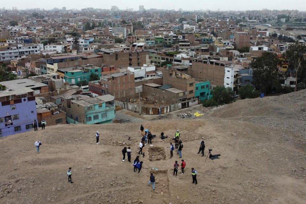 People stand near the excavation site of a pre-Hispanic burial with a mummy, believed to be from the Manchay culture which developed in the valleys of Lima between 1,500 and 1,000 BCE, in Lima, Peru, June 14, 2023.