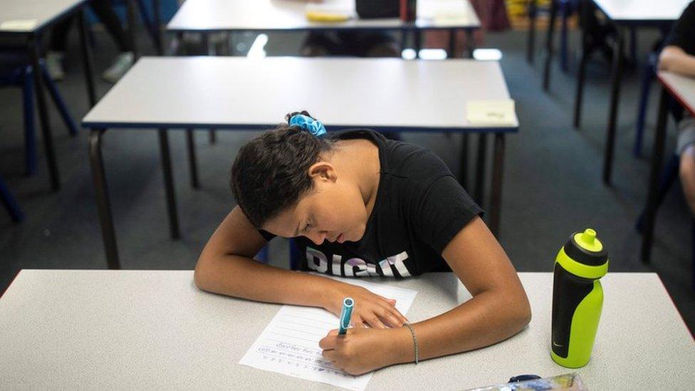 Girl sits at desk alone working after returning to socially distanced classroom