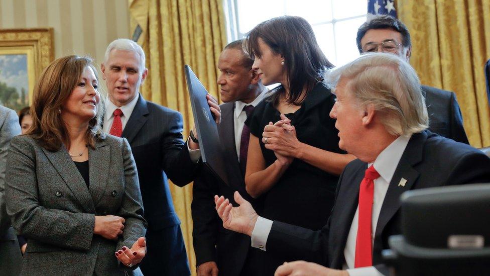 President Donald Trump hands off an executive order to Vice President Mike Pence, left, after signing the order in the Oval Office of the White House in Washington, Monday, Jan. 30, 2017, surrounded by small business leaders.