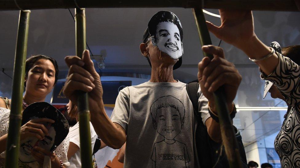 Activists stand behind makeshift bars wearing masks of Thai human rights activist Jatupat Boonpattararaksa, who was arrested in December 2016, 22 June 2017