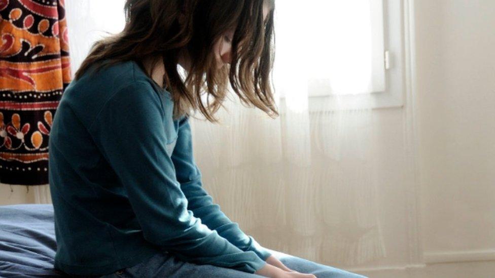 A young girl sitting on a bed, looking sad