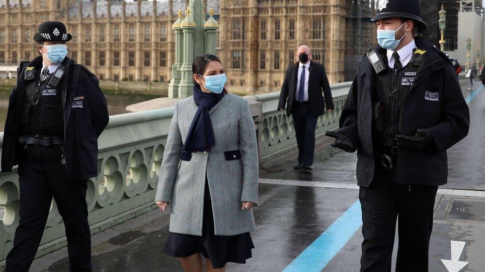 British Home Secretary Priti Patel walks with two police officers