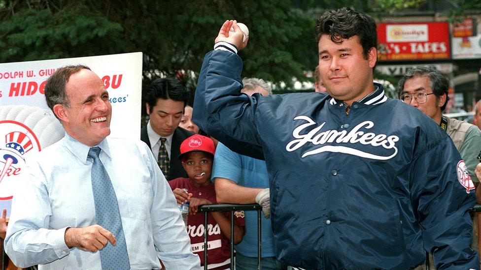 New York Yankees pitcher Hideki Irabu (R) shows his form to New York City Mayor Rudolph Giuliani at a city hall ceremony in New York