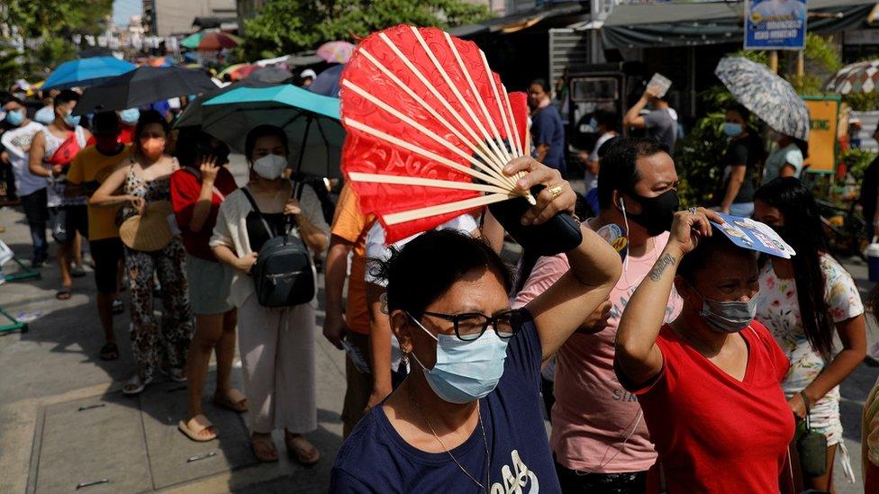 Filipinos hold fans while queuing on the street outside a polling precinct in Metro Manila