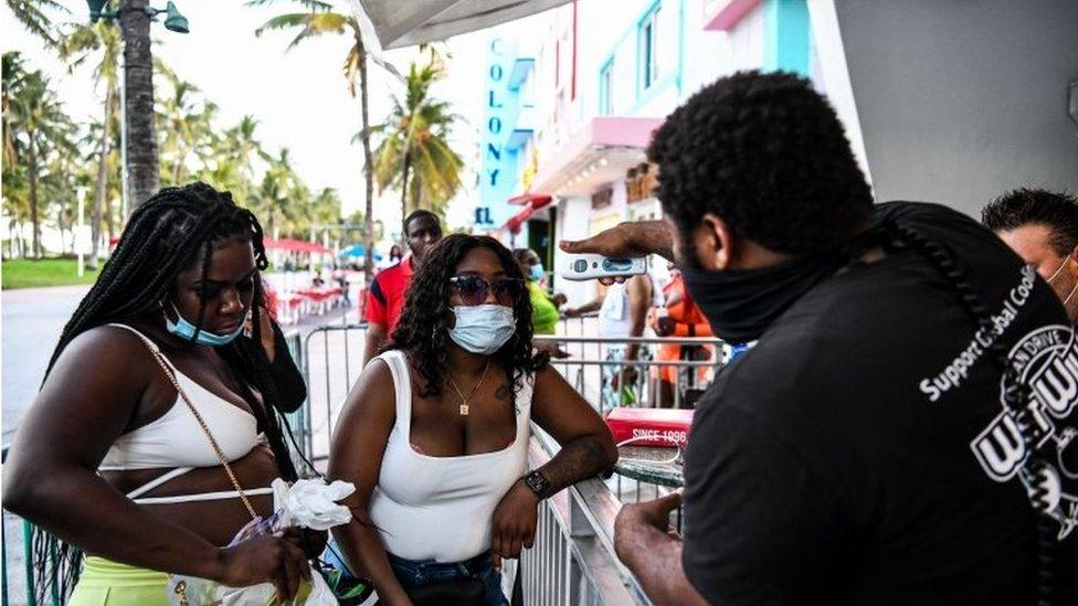 A security guard checks the temperature of a woman at the entrance of a restaurant on Ocean Drive in Miami Beach, Florida on June 24, 2020