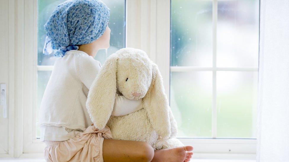 A girl with cancer sitting in a window