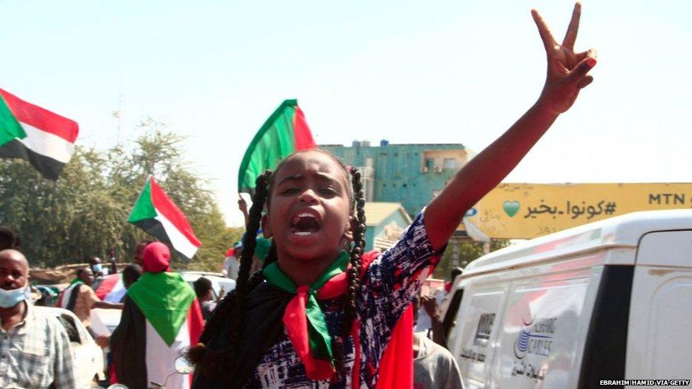 A young girl making a peace sign with Sudanese flags in the background