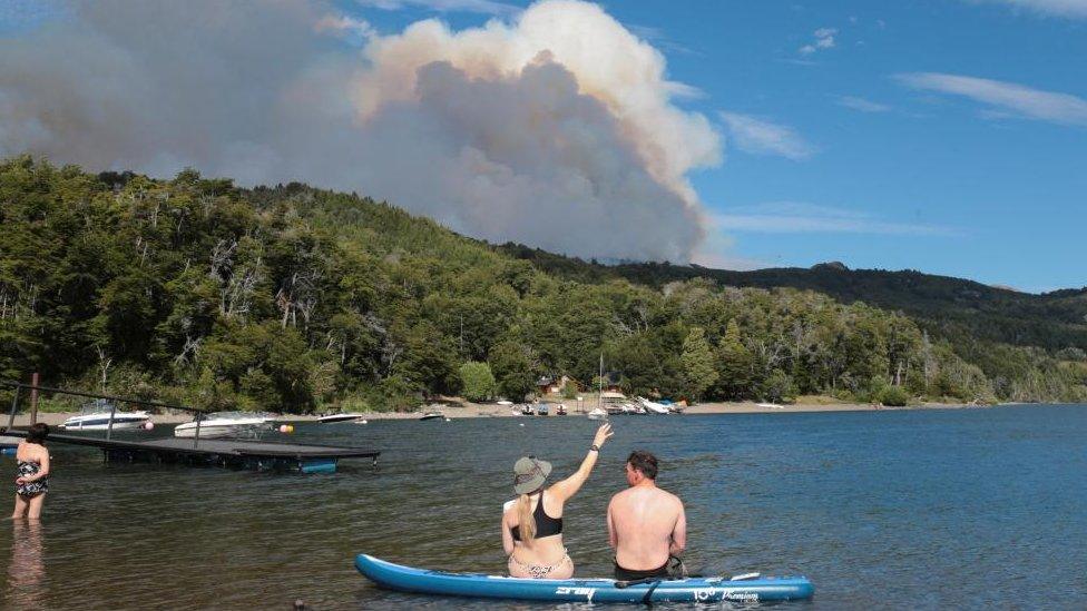 Tourists enjoy the day at the Futalaufquen Lake as smoke rises from trees as a wildfire burns at Los Alerces National Park, in Chubut, Argentina January 28, 2024.