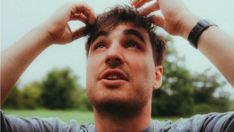 James Humphrys press shot - he is holding his hands to his head and looking up