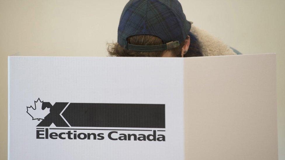 A voter casts a ballot behind an 'Elections Canada' sign.