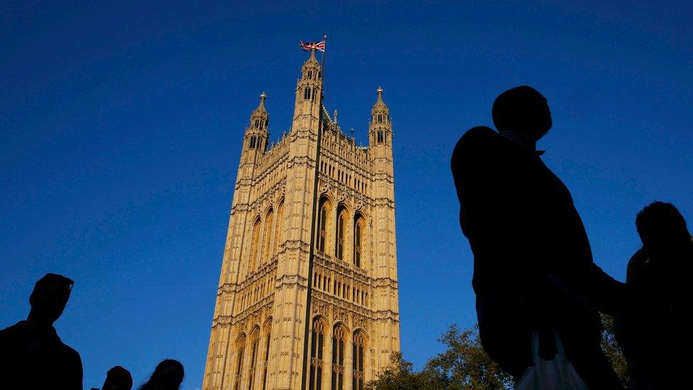 Silhouetted people walk past the Houses of Parliament