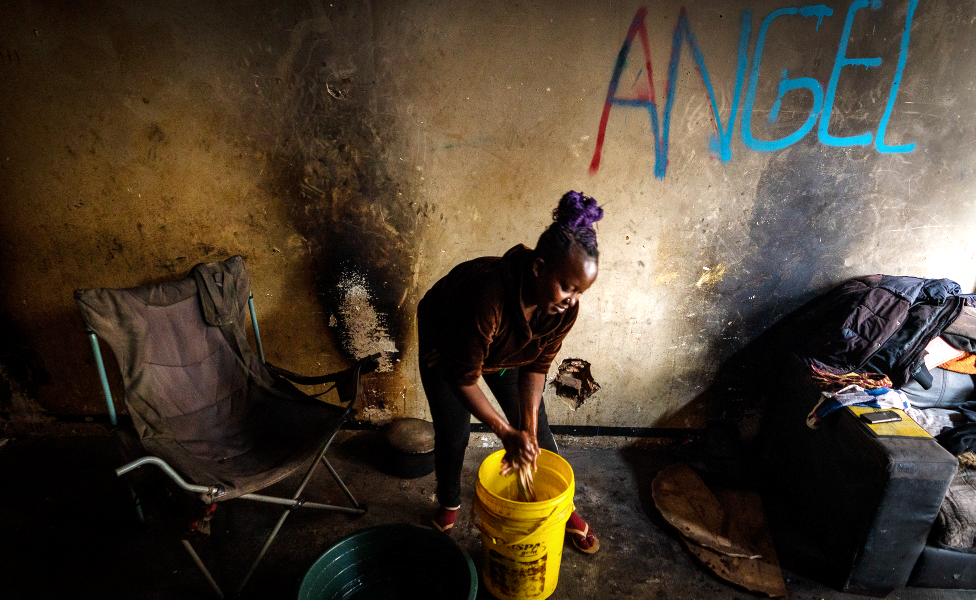 Angela doing her daily chores, washing clothing from a plastic bucket in the derelict San Jose building in Johannesburg, South Africa