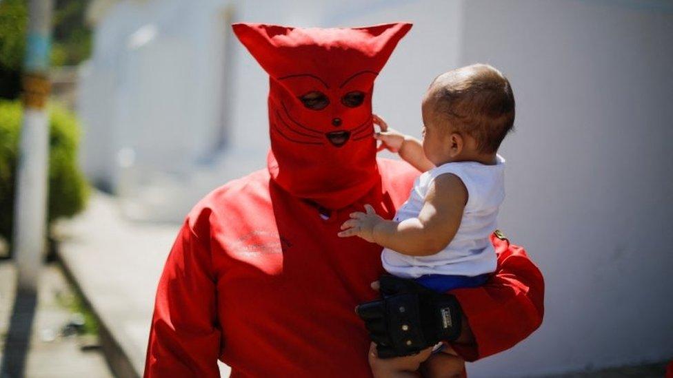 A man dressed as a demon holds his son as he participates in a ceremony known as Los Talciguines, as part of religious activities to mark the start of the Holy Week in Texistepeque, El Salvador, April 11, 2022.