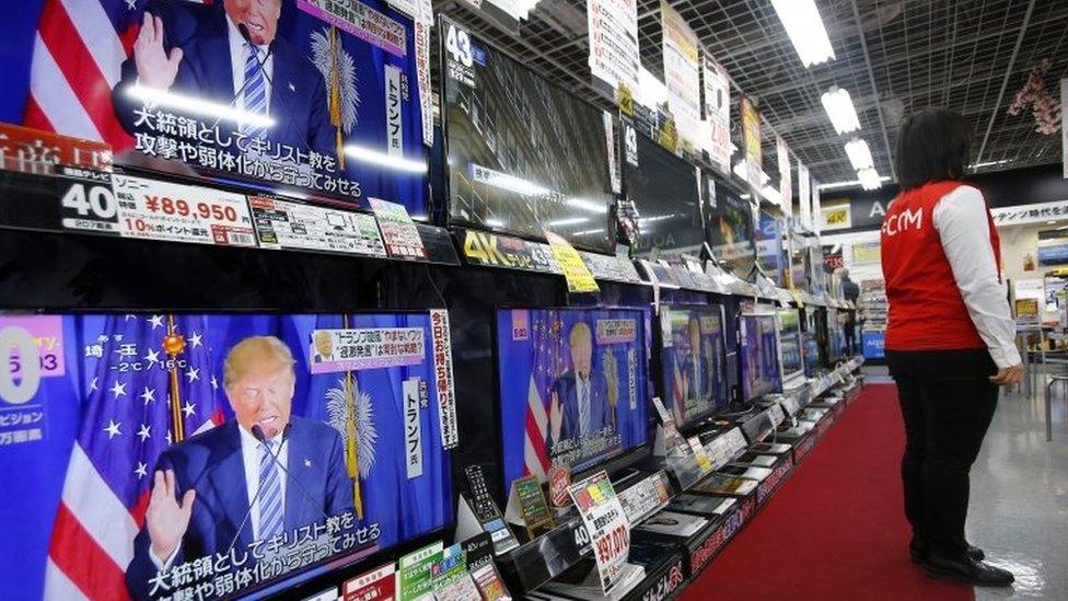 A salesclerk stands in front of flat-panel TVs showing Republican front-runner candidate Donald Trump at an electronics store in Tokyo, on 2 March 2016