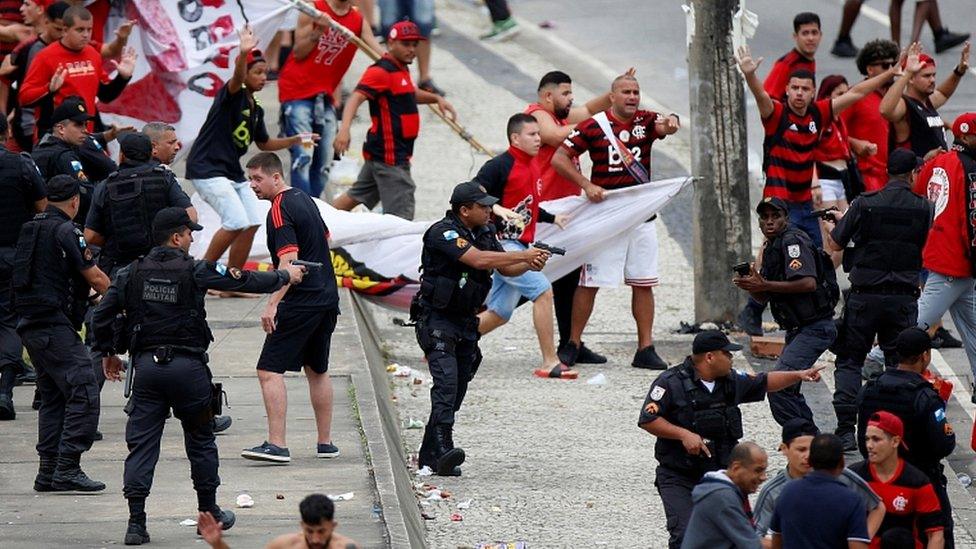 Rio police draw their weapons during clashes with fans at the parade