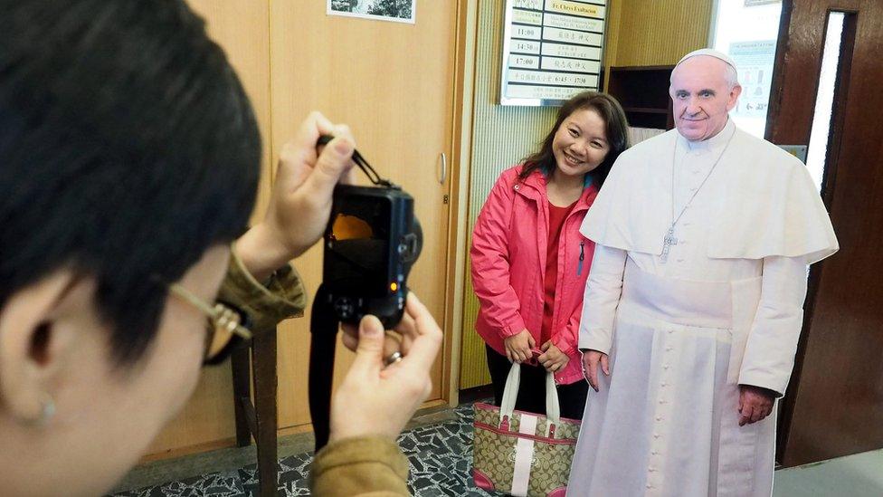 A woman poses for a photograph next to a paper cutout of Pope Francis in the Holy Family Catholic Church in Taipei, Taiwan