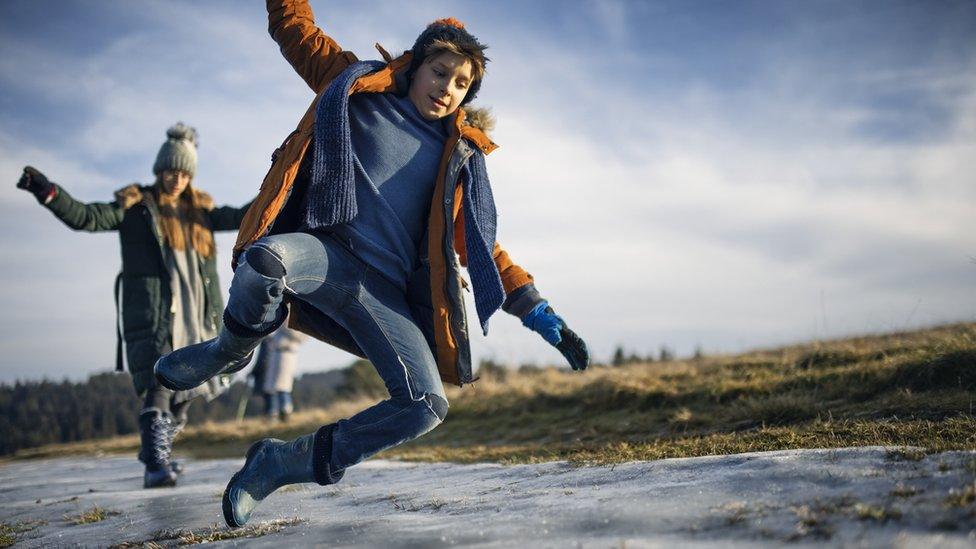 a child jumps over a patch of ice while a girl walks carefully behind them